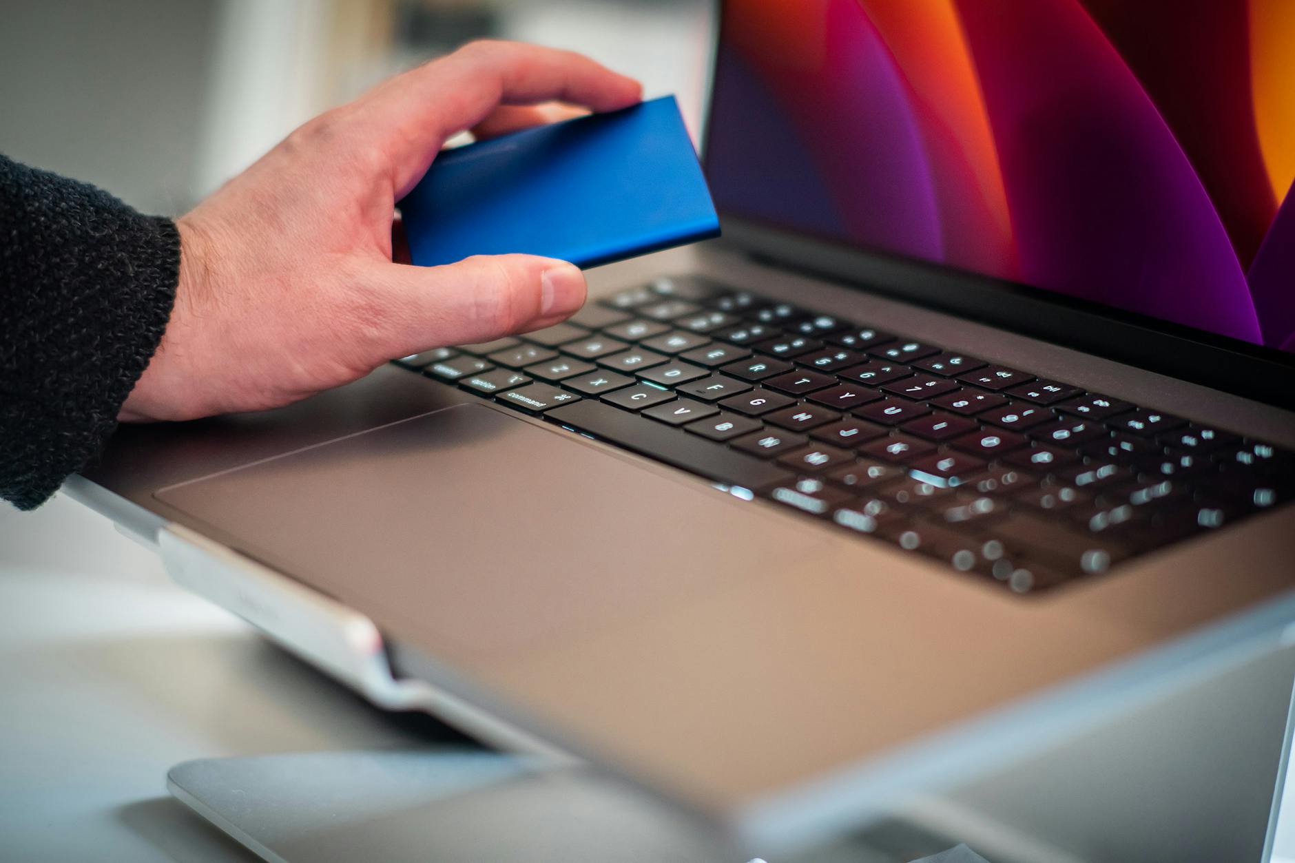 Dłoń trzyma zewnętrzny dysk twardy nad klawiaturą laptopa