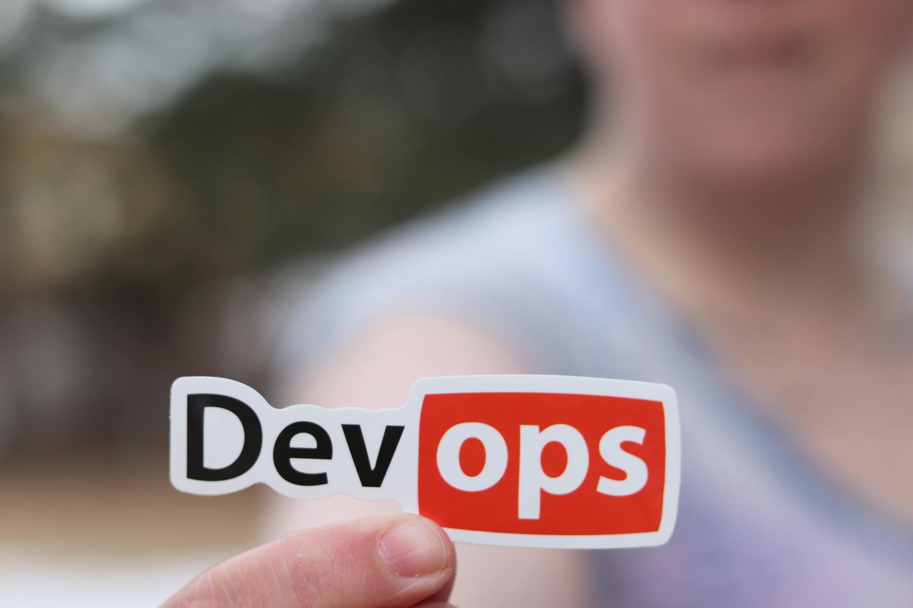 Dłoń trzymająca naklejkę DevOps w otwartej przestrzeni na zewnątrz
