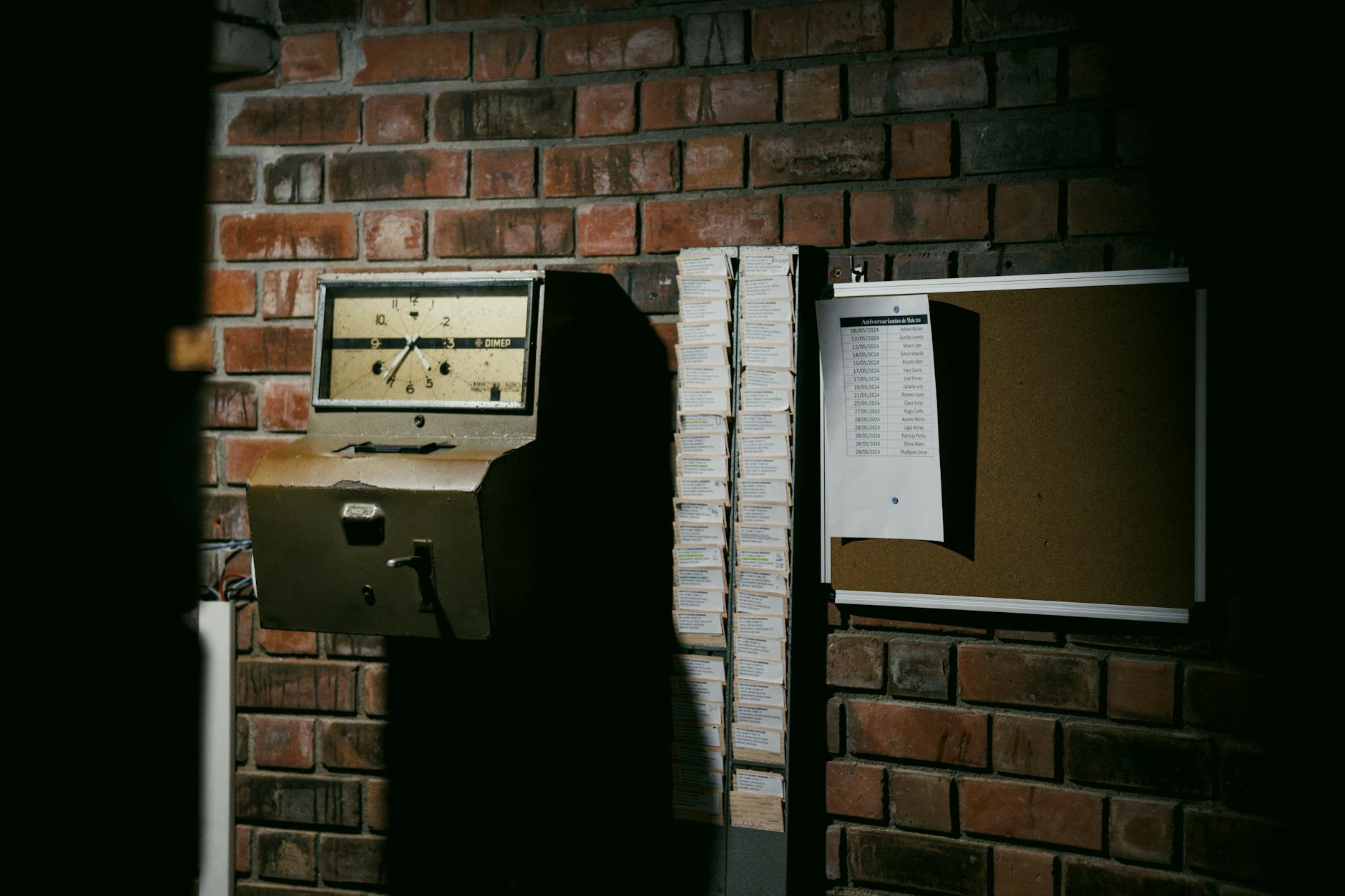 Zegar przemysłowy i stos kart perforowanych na tle ceglanej ściany